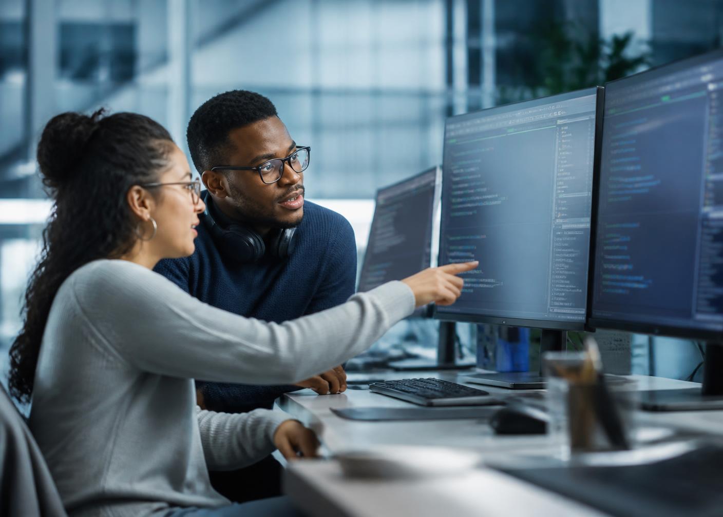 Two software engineers reviewing code together on large monitors in a modern office